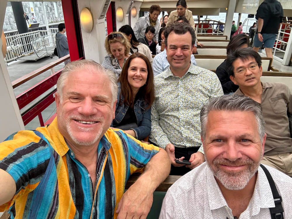 A group of five people smiling and taking a photo while on a boat ride. The mood is joyful.