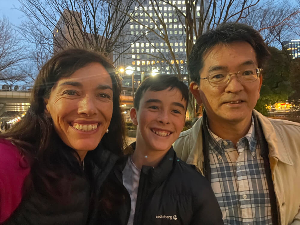 Three people taking a selfie together with a city nightscape in the background. Their smiles are prominent.