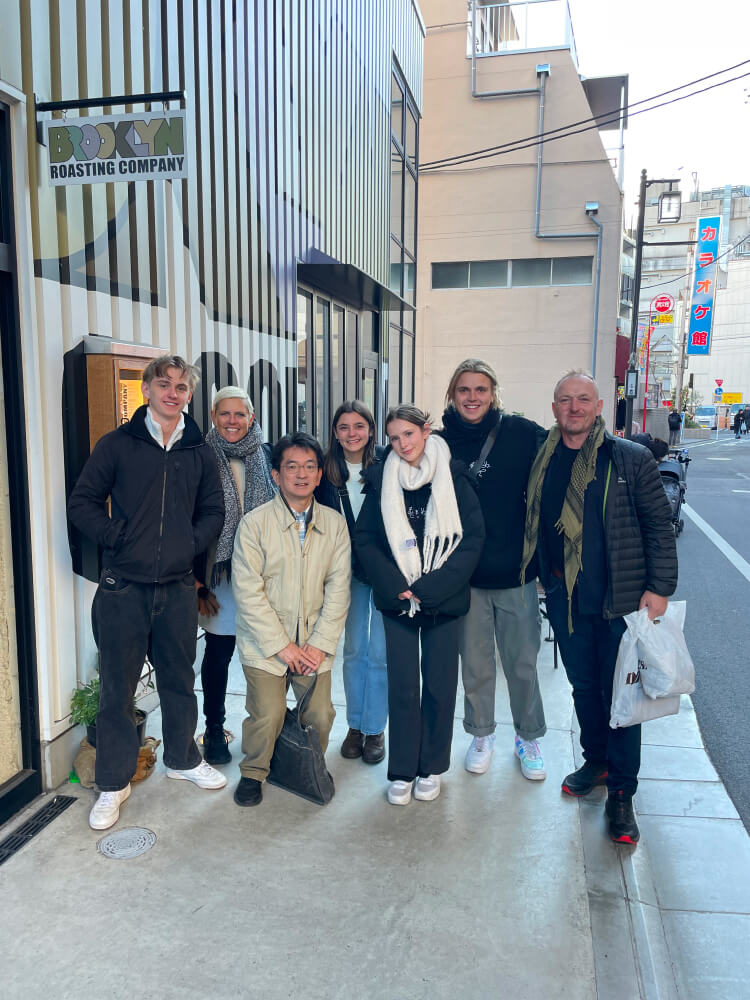 A group of seven people posing outside a coffee shop. The atmosphere is relaxed.