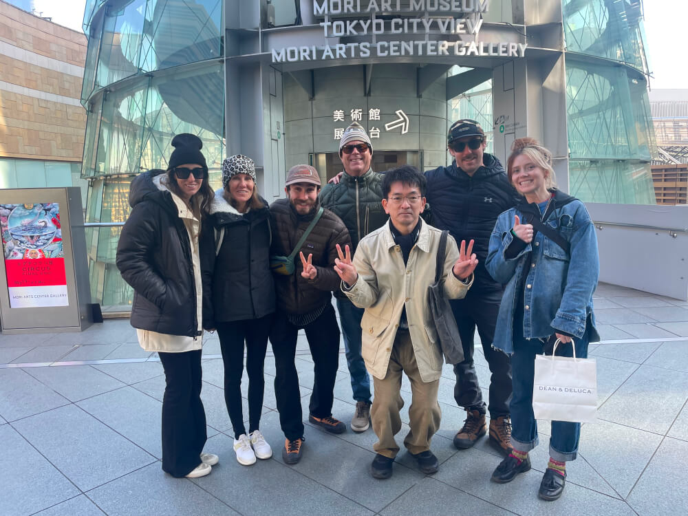 A group of six people posing in front of the Mori Art Museum. It's a moment from their sightseeing.