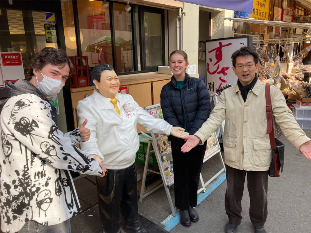 A group of three people taking a photo with a famous character statue on the street. They are smiling and striking a humorous pose.