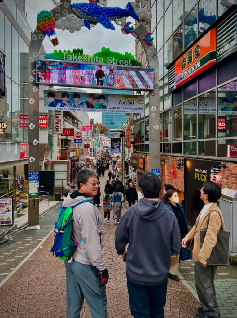 People walking on Takeshita Street in Harajuku. The street is bustling with tourists, giving off a lively shopping district vibe.