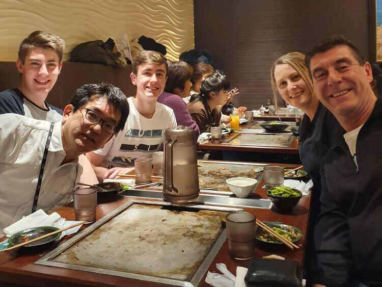 A group of five people enjoying a meal at a teppanyaki restaurant. They are smiling and posing for the camera.